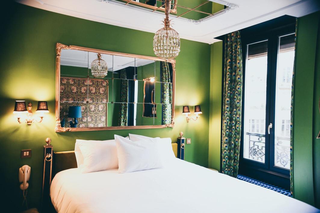 chambre avec lit double, miroir au dessus du lit et murs verts à l'hôtel soleil du matin